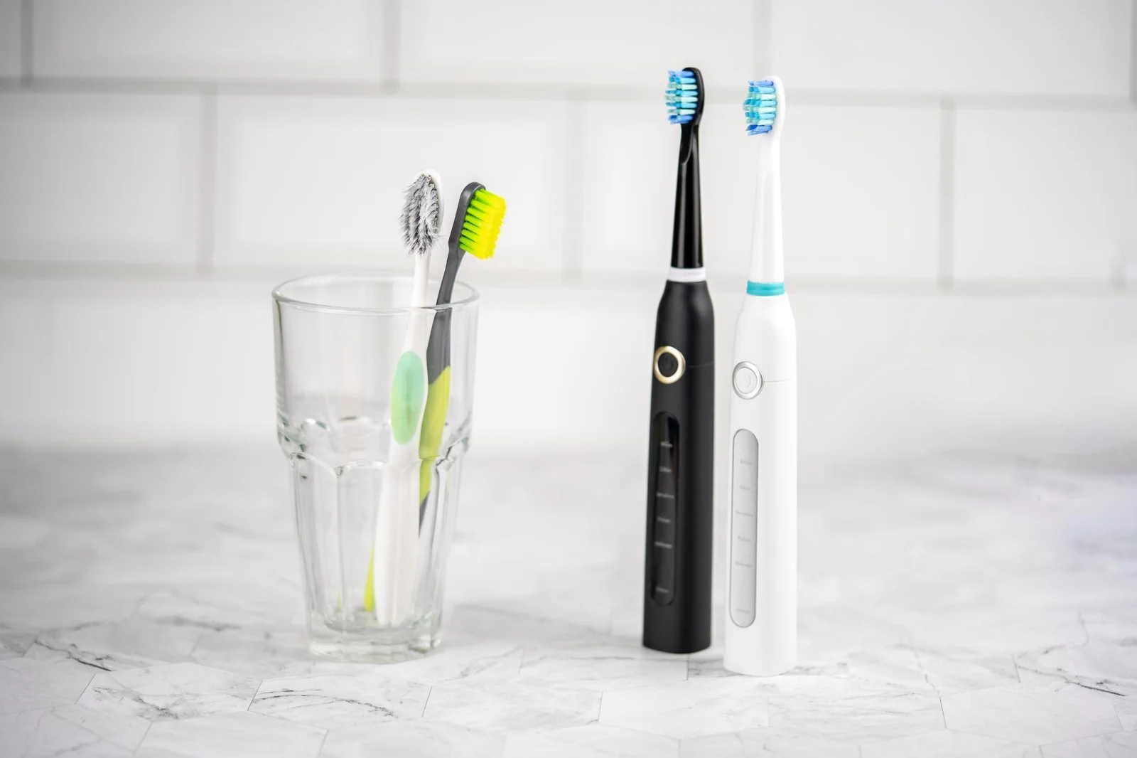 Manual toothbrushes in a glass beside two electric toothbrushes