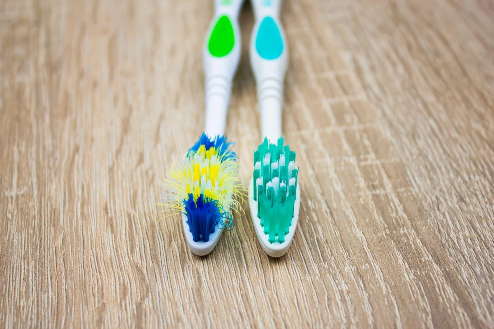 A toothbrush with frayed bristles beside a toothbrush with upright bristles